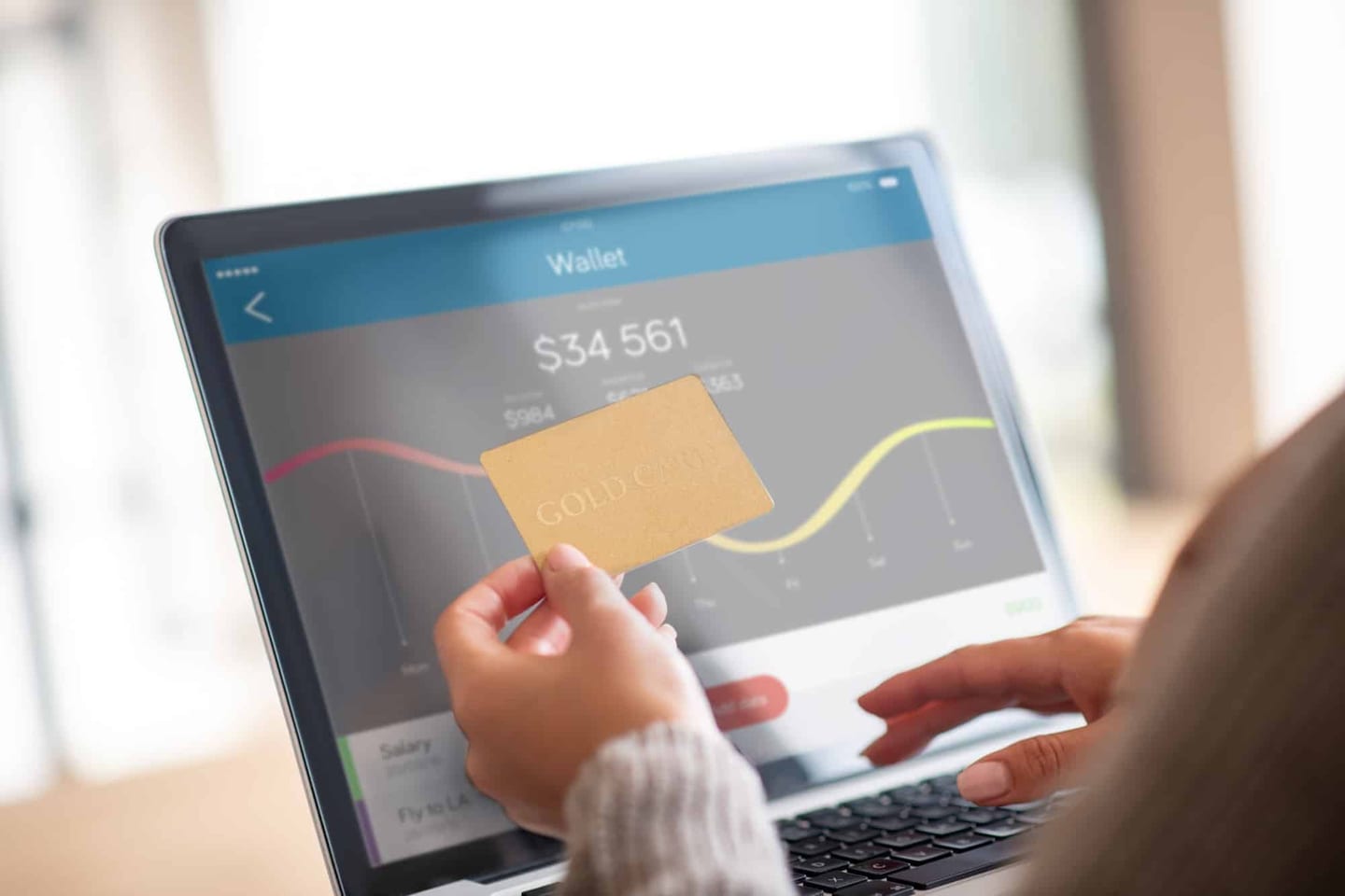 A woman holding a tablet that shows a bank-account balance and a credit card — close-up of the hands