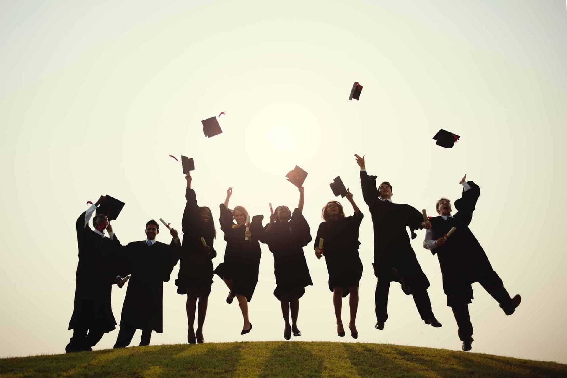 Graduates in gowns throwing their caps into the air, silhouetted against a sunset