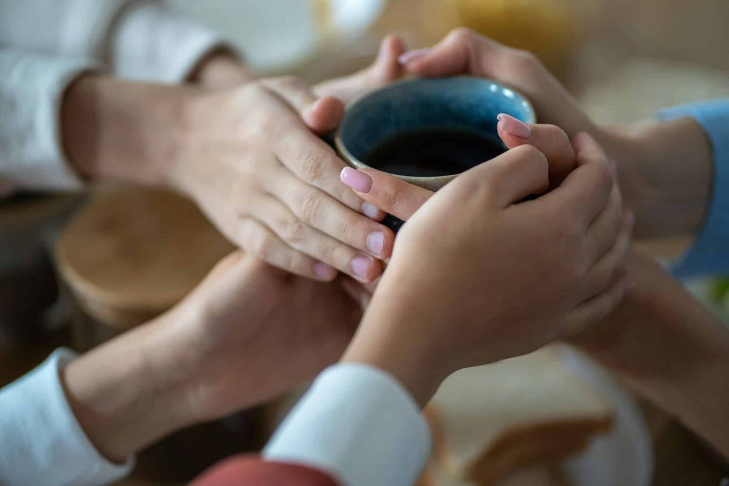 Family members' hands holding a cup of hot tea together — close-up