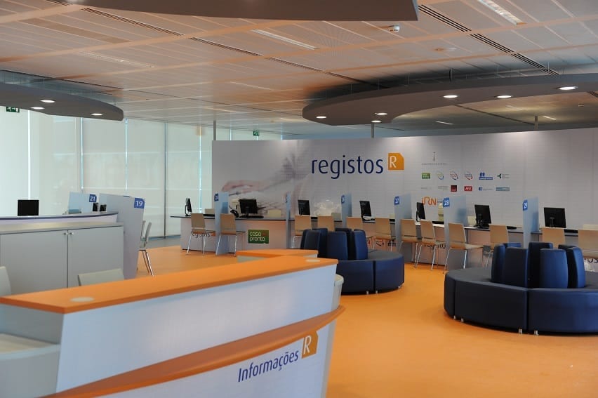 Inside an IRN office (Instituto dos Registos e do Notariado) — a registos counter and orange waiting chairs