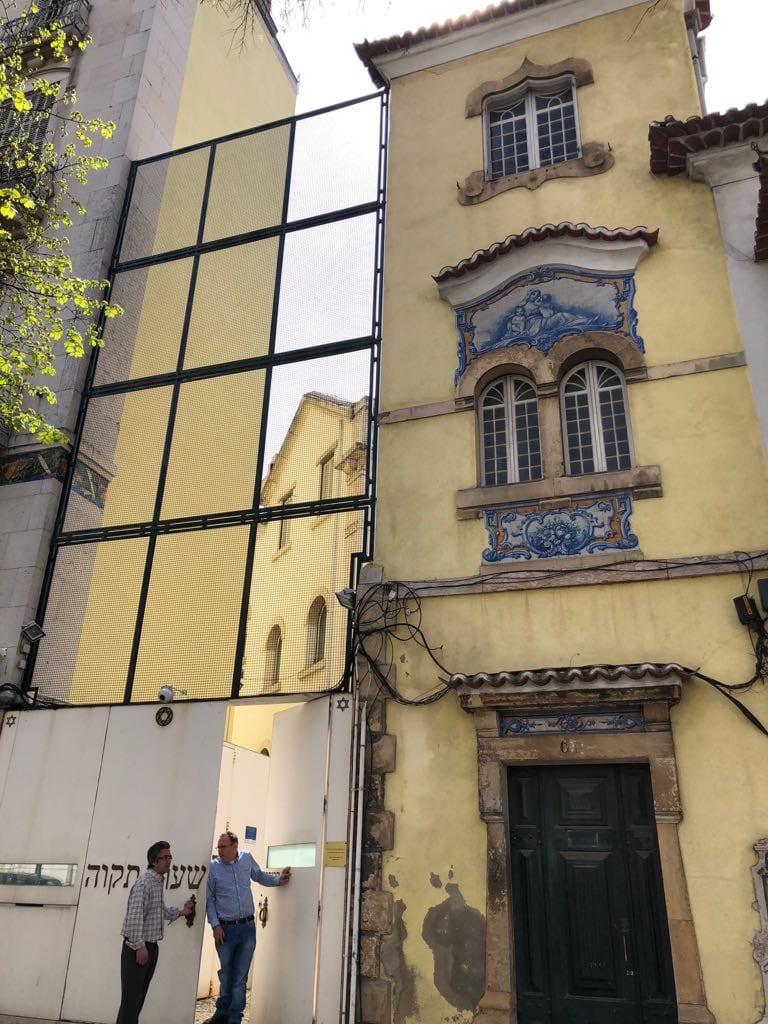 Facade of the Shaare Tikva synagogue in Lisbon seen from a narrow street — a light stone building with arched windows
