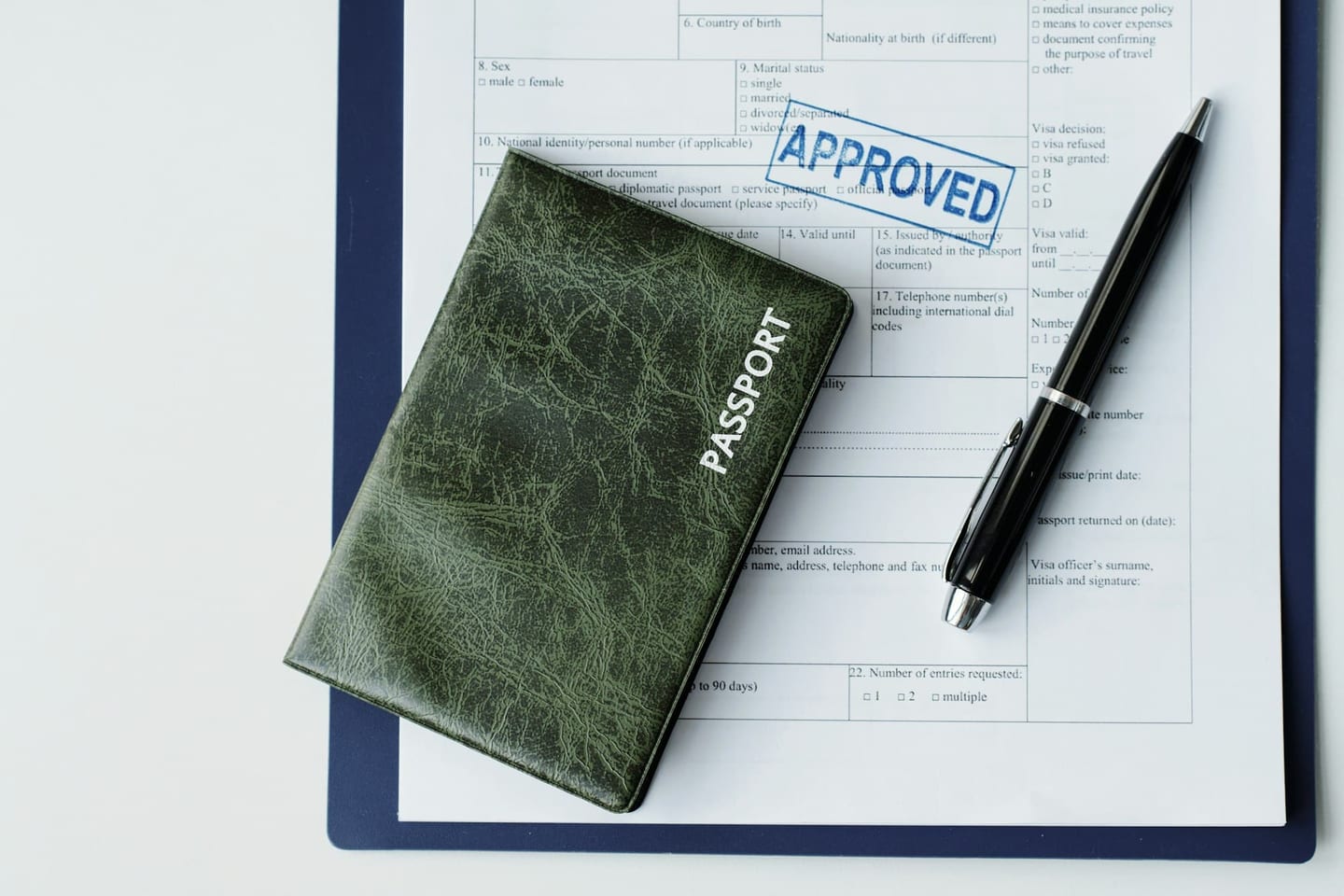 A green passport, a pen and a form stamped APPROVED in blue on a desk