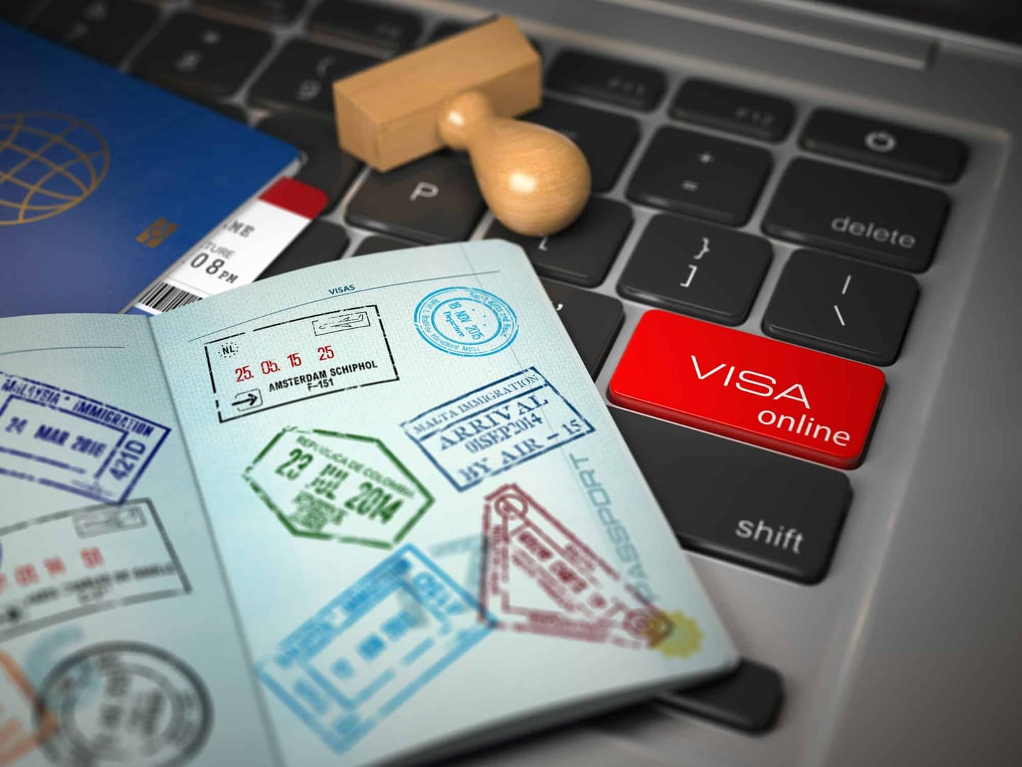 An open passport with visa stamps, a red VISA online key and a wooden stamp on a computer keyboard
